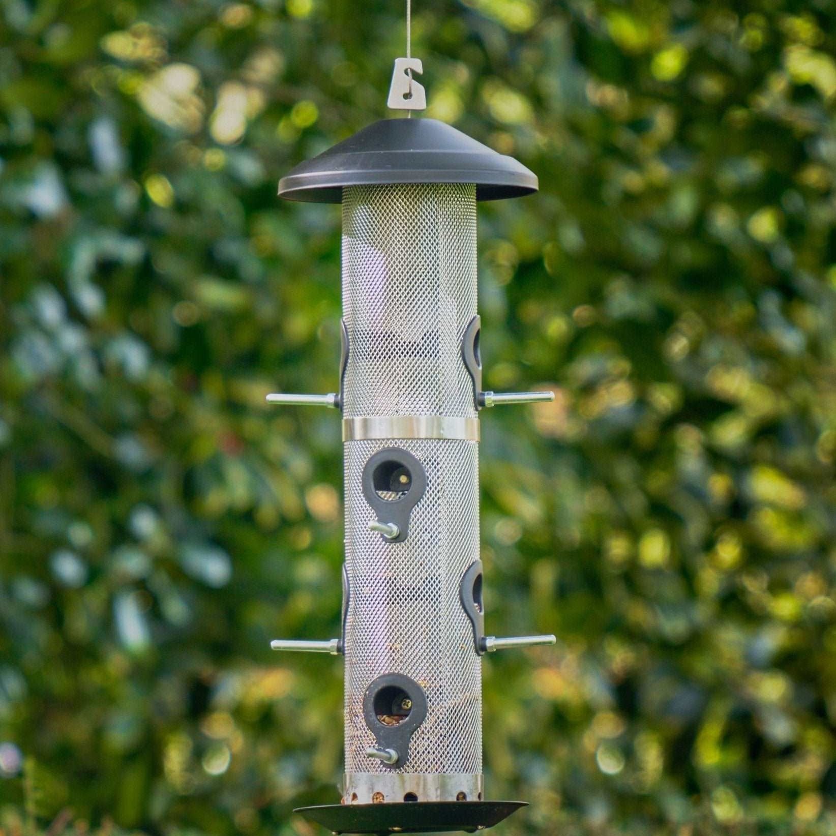 Giant Bird Seed Feeder - The Irish Gardener Store Giant bird seed feeder, tall cylindrical design, metal mesh body, black weather-resistant top and base, multiple feeding ports with perch attachments, hanging wire for easy installation, ideal for attracting multiple bird species