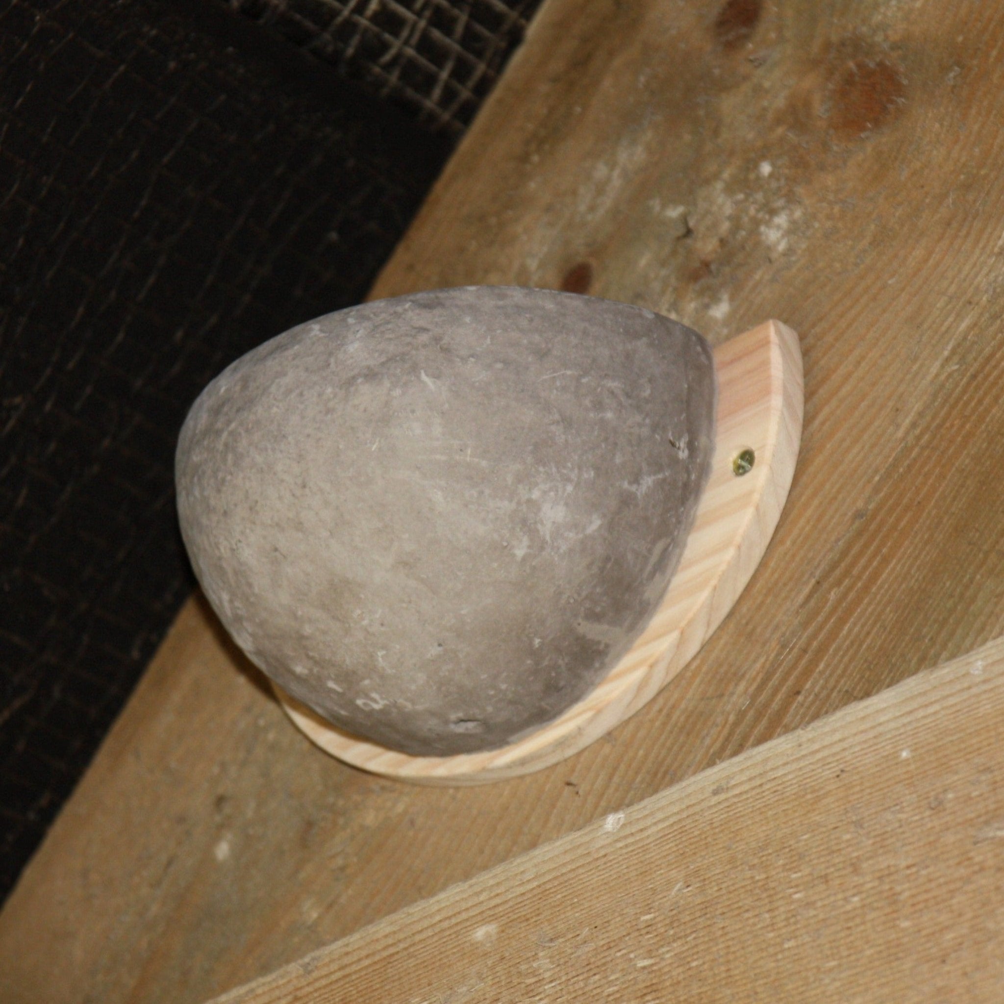 Close-up of a ceramic swallow nesting bowl mounted on a wooden base, securely attached to a wooden beam, designed to provide a safe nesting spot for swallows