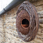 Simon King Wreath Nester - The Irish Gardener Store Simon King Wreath Nester made of natural twigs and branches, rustic bird nester attached to a stone wall, eco-friendly wildlife habitat, handcrafted wreath design, perfect for small birds, sustainable nesting solution, outdoor decorative garden feature, natural woven structure, ideal for birdwatching enthusiasts