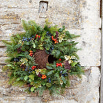 Simon King Wreath Nester - The Irish Gardener Store Simon King Wreath Nester hanging on a stone wall, adorned with natural foliage and berries, eco-friendly bird nester, decorative wildlife habitat, rustic garden feature, sustainable nesting solution for small birds, handcrafted wreath design, outdoor bird-friendly accessory, vibrant greenery and colorful berries
