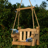 Swingseat Bird Feeder - The Irish Gardener Store natural wooden swingseat bird feeder, hanging bird feeder on ropes, rustic garden decor, wooden swing bird feeder for seeds, outdoor bird feeding station, eco-friendly bird feeder hanging in garden, bird feeder in countryside setting, handcrafted wooden swing bird feeder