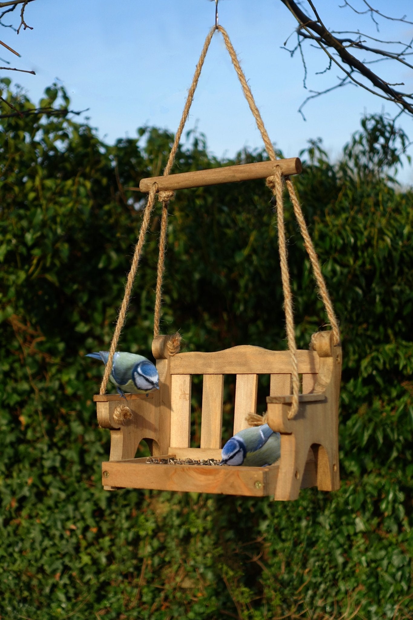 Swingseat Bird Feeder - The Irish Gardener Store natural wooden swingseat bird feeder, hanging bird feeder on ropes, rustic garden decor, wooden swing bird feeder for seeds, outdoor bird feeding station, eco-friendly bird feeder hanging in garden, bird feeder in countryside setting, handcrafted wooden swing bird feeder
