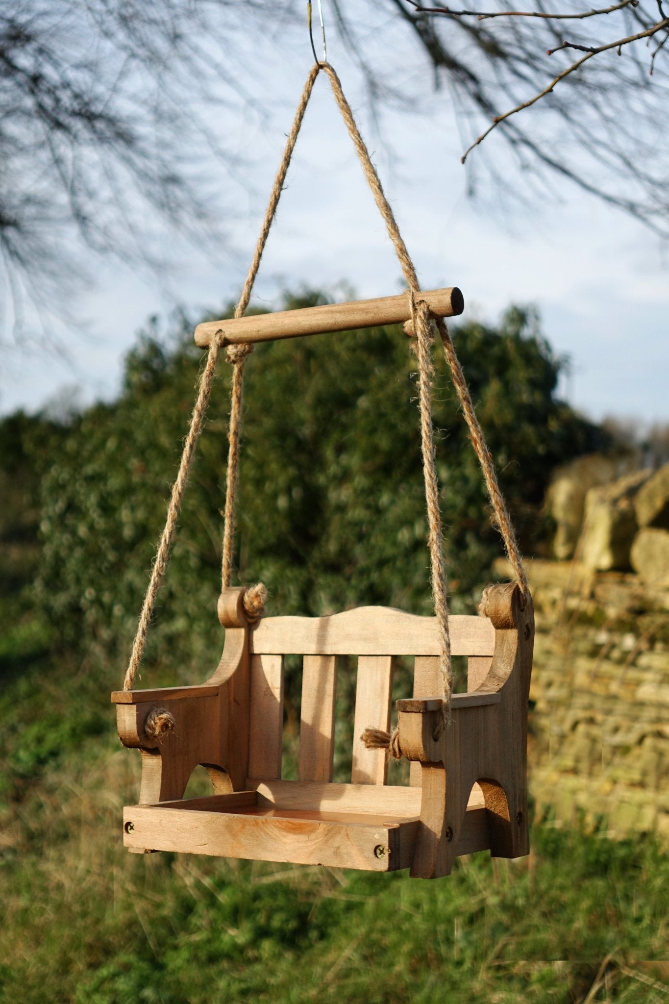 Swingseat Bird Feeder - The Irish Gardener Store natural wooden swingseat bird feeder, hanging bird feeder on ropes, rustic garden decor, wooden swing bird feeder for seeds, outdoor bird feeding station, eco-friendly bird feeder hanging in garden, bird feeder in countryside setting, handcrafted wooden swing bird feeder