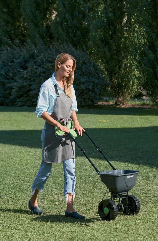 Image of the Verdemax Rotary Fertiliser Spreader, showcasing its sturdy construction and ergonomic design. The spreader is depicted being used in a garden, dispersing fertiliser evenly across the soil