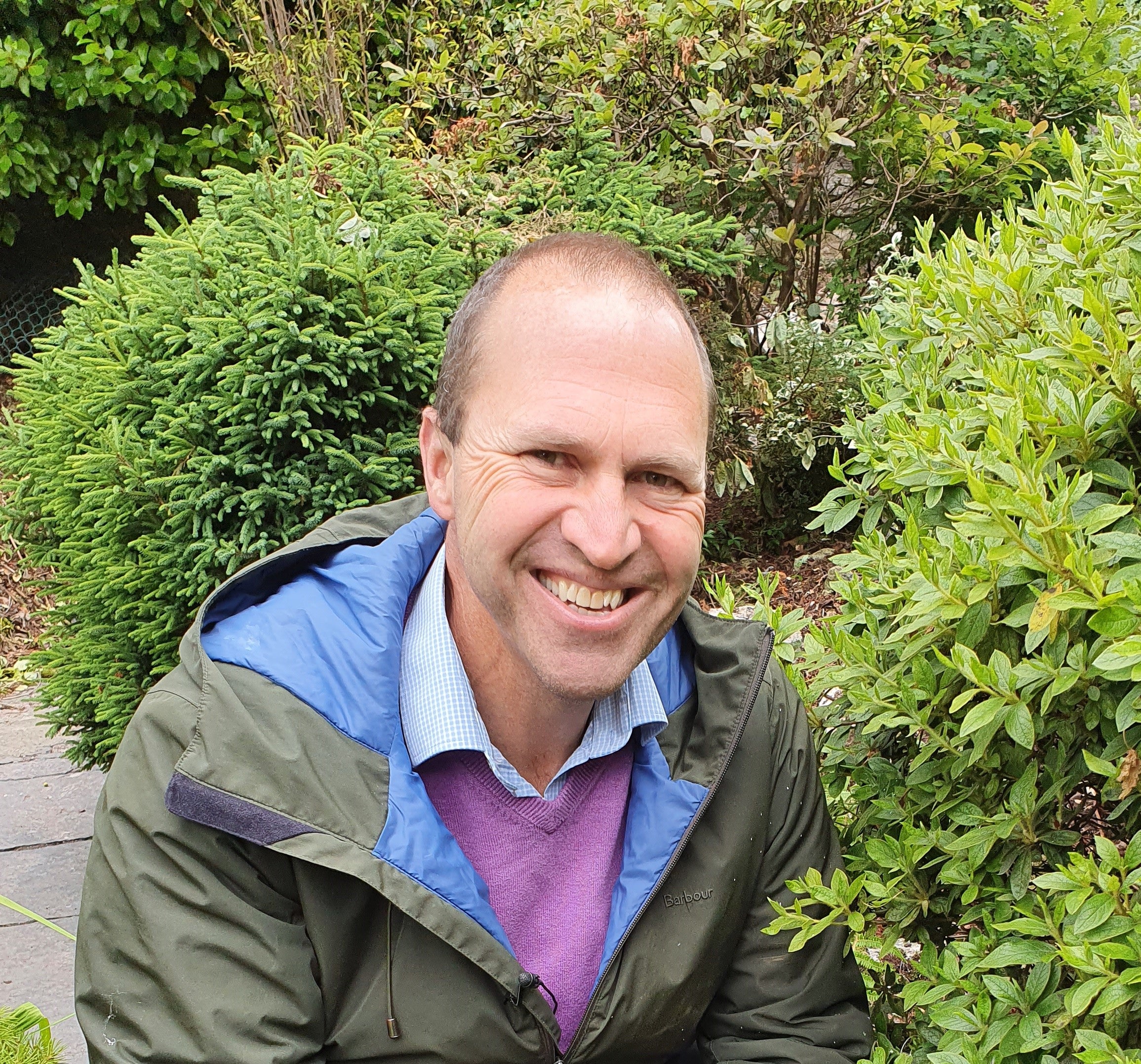 Peter Dowdall smiling outdoors with greenery in the background