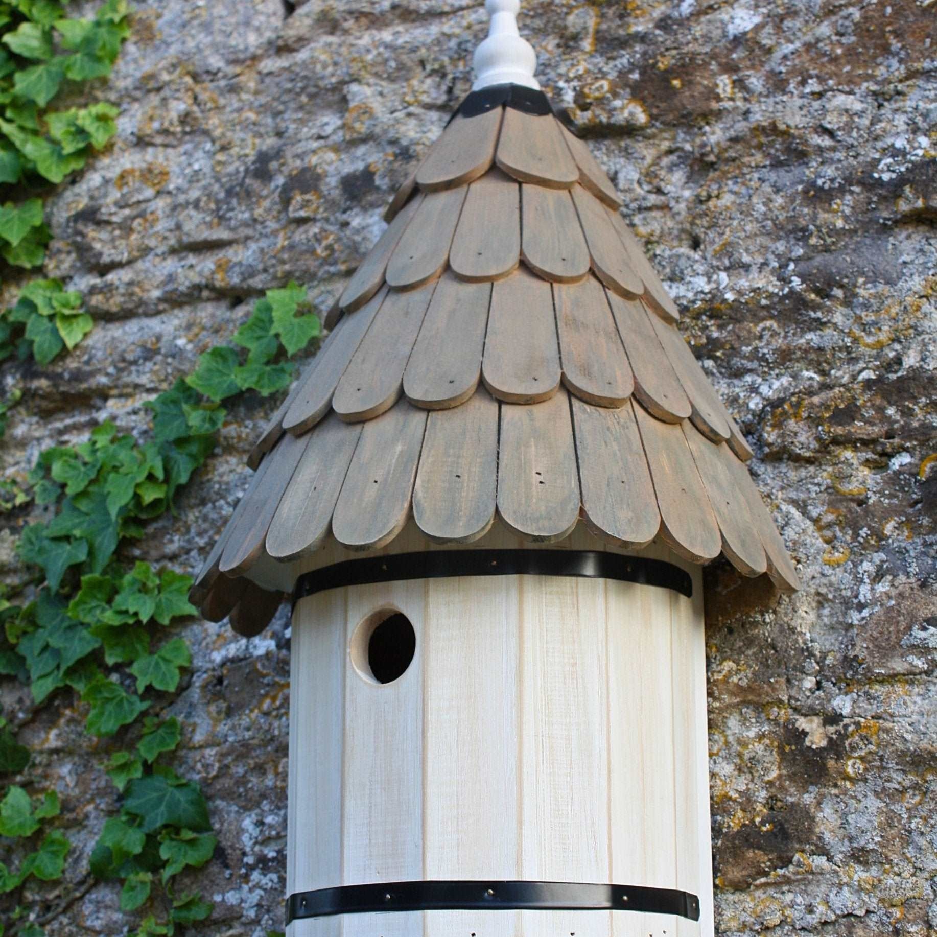 Dovecote Nest Box - The Irish Gardener Store Wooden dovecote nest box, featuring a traditional round design, scalloped wooden roof with natural finish, small circular entry hole, decorative white finial on top, elegant and rustic birdhouse design