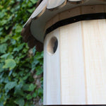 Dovecote Nest Box - The Irish Gardener Store Wooden dovecote nest box, featuring a traditional round design, scalloped wooden roof with natural finish, small circular entry hole, decorative white finial on top, mounted against a backdrop of lush green ivy, elegant and rustic birdhouse design