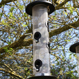 Giant Bird Seed Feeder - The Irish Gardener Store Giant bird seed feeder, tall cylindrical design, metal mesh body, black weather-resistant top and base, multiple feeding ports with perch attachments, hanging wire for easy installation, ideal for attracting multiple bird species