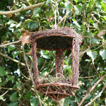 Open Nest Buddy - The Irish Gardener Store Open Nest Buddy, rustic woven design, crafted from natural twigs and moss, open-front structure, hanging from a tree branch, surrounded by green foliage, eco-friendly bird shelter, suitable for robins and other open-nesting birds, decorative and functional garden feature