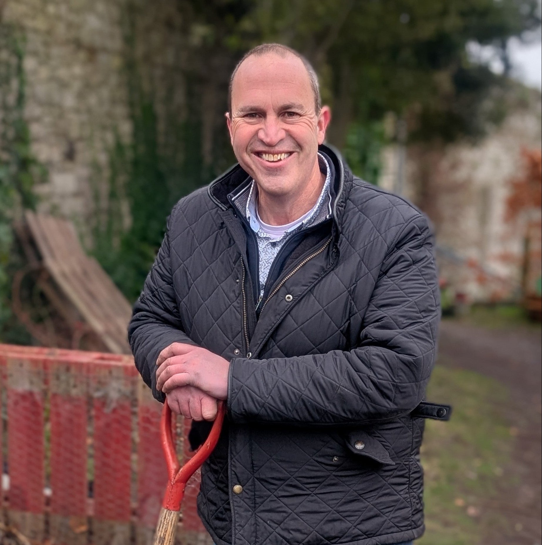 Garden expert Peter Dowdall holding a shovel in an outdoor setting with a red tool chest and greenery.