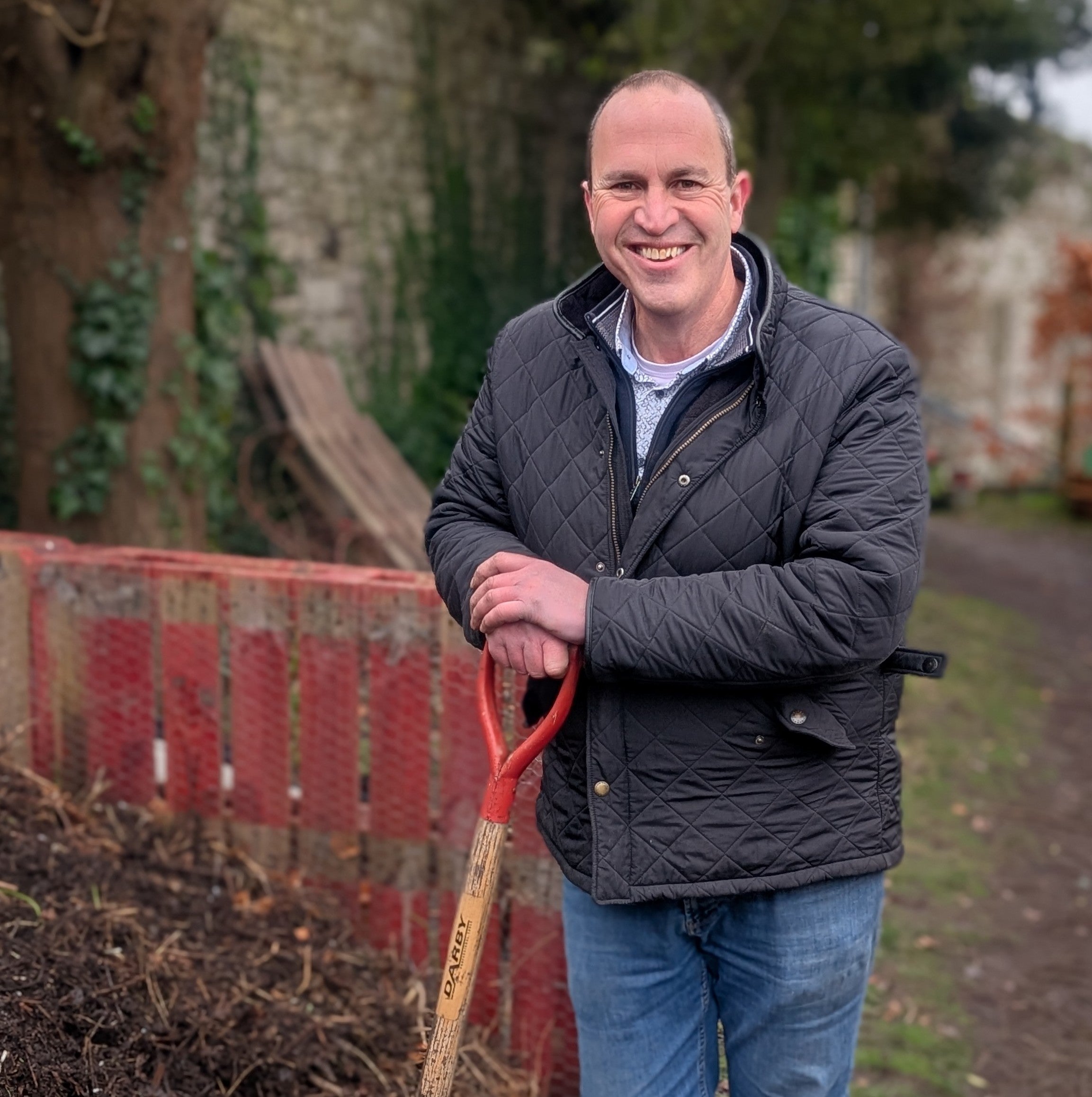 Peter Dowdall with a shovel standing next to compost bins