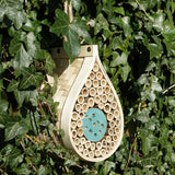 Dewdrop-shaped bee and bug hotel, made from natural wood, featuring bamboo tubes and wooden compartments, designed for solitary bees and beneficial insects, mounted on a garden wall, surrounded by greenery, eco-friendly insect habitat, rustic garden decoration